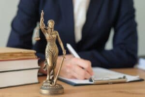 woman at desk writing on clipboard next to statuette of lady justice