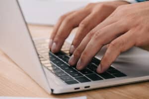 closeup of man's hands typing on laptop on a wooden table